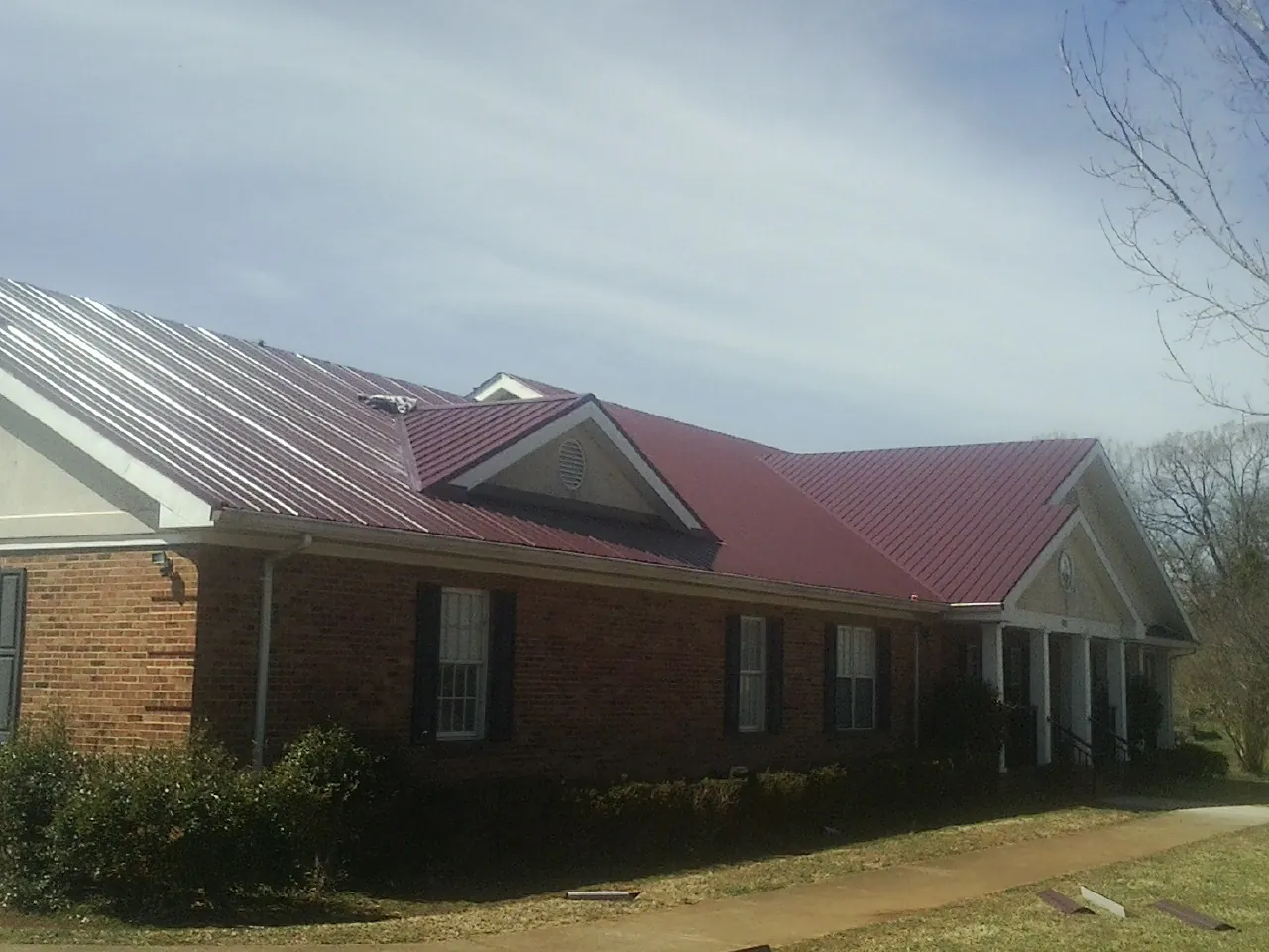 Red metal roof with gabled entries on a long brick building, from a Hail Damage Roof Repair job in West Orange