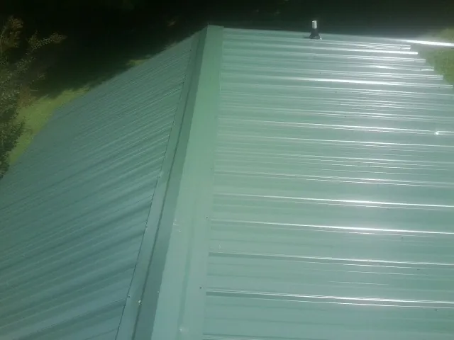 New green metal panels meeting at the ridge of a roof — Flat Roof Repair work by our crew in West Orange