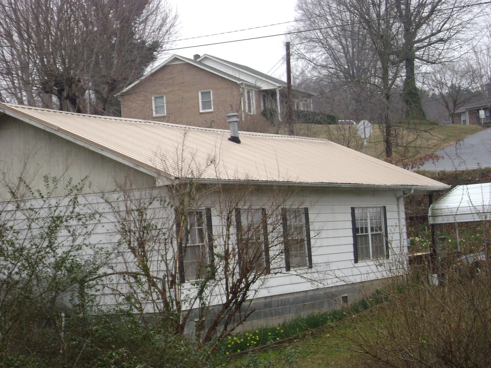 Tan metal roof on a white sided house set into a hillside — Commercial Roofing by Roofing Brothers in West Orange